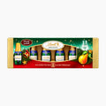 A Lindt Alcohol Specialties Bottles Williams gift set containing four mini chocolate bottles, presented in a decorative gold and green box with festive illustrations of pine branches, a pear, and a brandy glass.