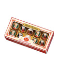 A box of Reber Assorted Kugeln pralines, with each praline individually wrapped in gold and red foil. The box is filled with pralines made with dark and alpine milk chocolate, filled with hazelnut nougat, marzipan, pistachio marzipan, and cream truffle.