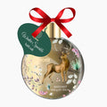 A decorative bath salt bauble shaped like a Christmas ornament, featuring a gold deer illustration, floral details, a red ribbon bow, and a green hanging tag that reads 'Winter Sparkle bath salt' on a light gray background.
