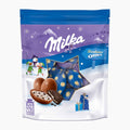 A package of Milka Bonbons Oreo chocolate eggs in a decorative winter-themed stand-up pouch. The packaging features a blue and purple snowy mountain background with the white 'Milka' logo, a star-shaped window showing blue chocolate eggs with gold stars, and illustrations of snowman figures, gifts, and an opened chocolate egg with Oreo cookie filling.