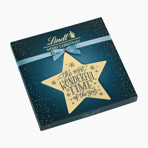 Lindt Merry Christmas Calligraphy chocolate pralines box in dark teal blue with gold speckles, a light blue ribbon, and a large gold star reading 'the most wonderful time of the year'.