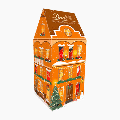 Lindt Christmas Large House chocolate pralines box, featuring a detailed gingerbread house design with festive windows, lights, snow, and a decorated Christmas tree on a white background.