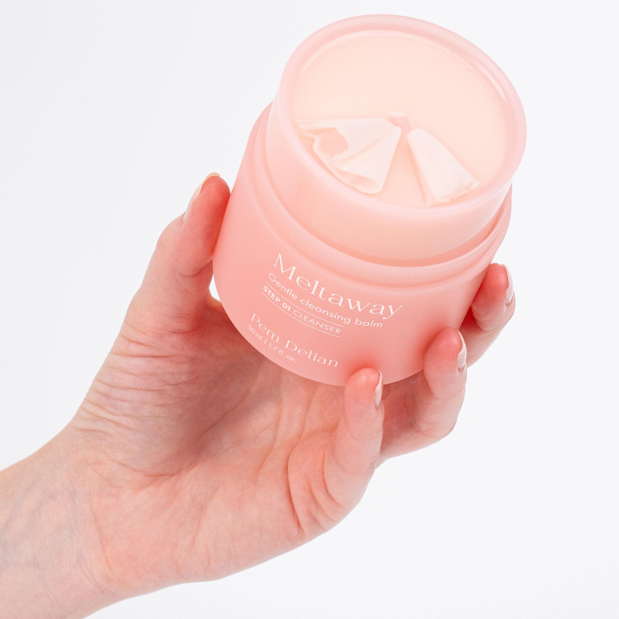 Hand holding a pink jar of 'Meltaway' cream against a light background