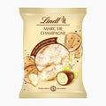 A package of Lindt Marc de Champagne Cones chocolate, featuring a cream-colored bag with elegant brown text and illustrations of chocolate truffles, a champagne glass, and grapes.