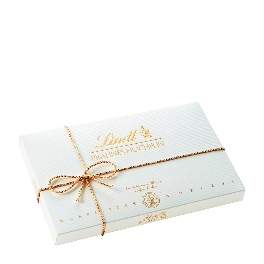 A box of Lindt Fine Pralines with a hand-tied ribbon on top, displaying various types of pralines such as Nut Nougat, Marc de Champagne Truffle, and more.