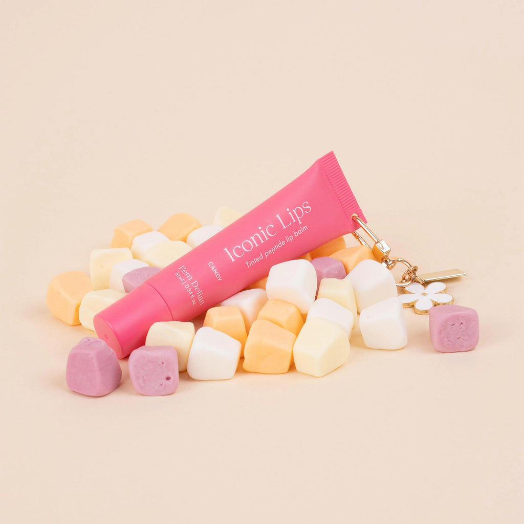 Pink lip balm tube with a charm on a beige background with colorful candies.