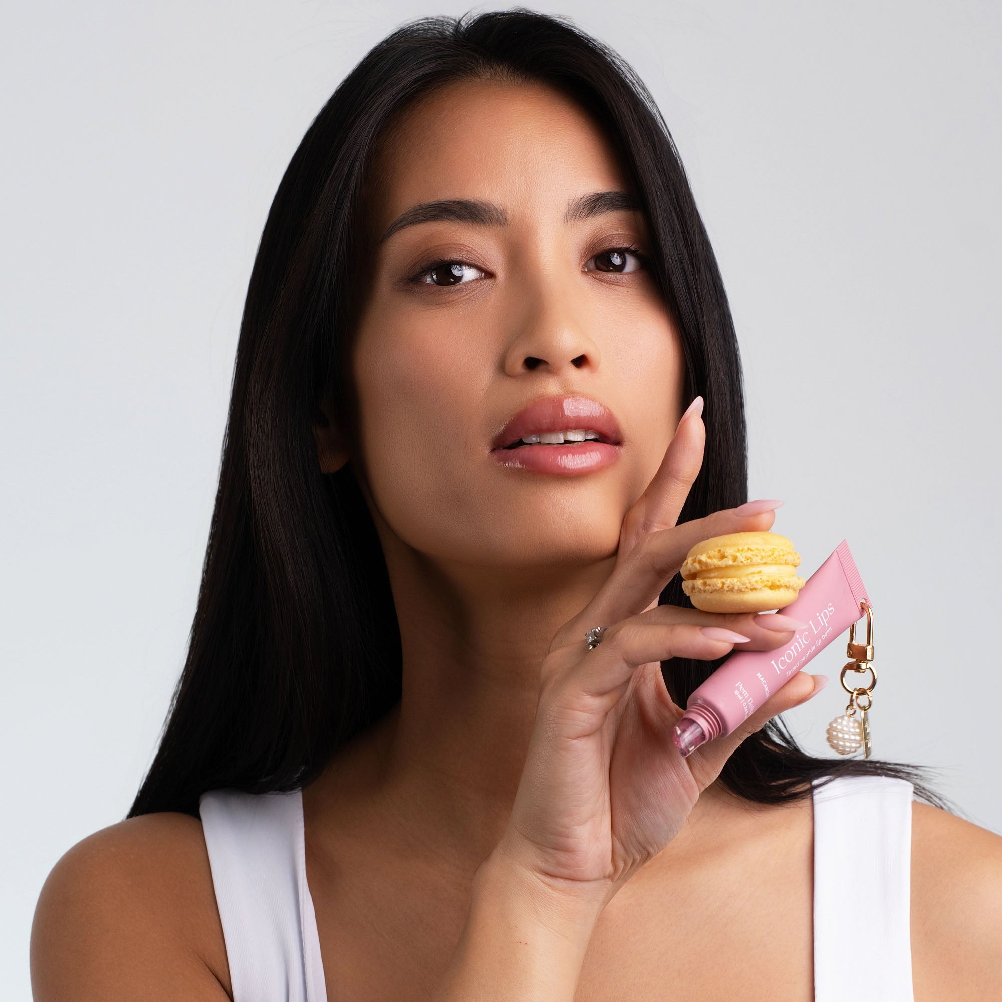 Woman holding a lip balm and a small yellow macaron against a plain background