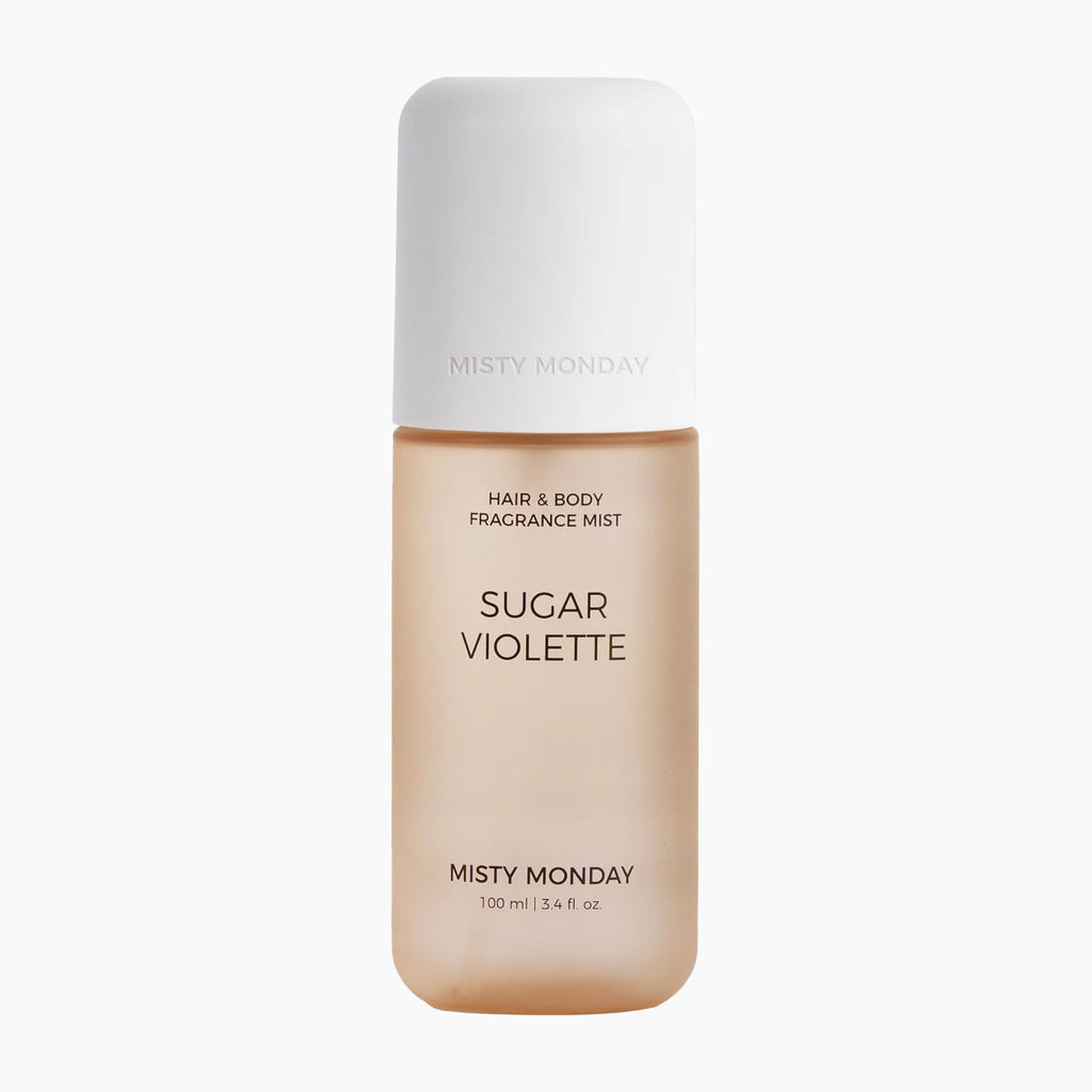A bottle of Misty Monday Sugar Violette hair and body fragrance mist, featuring a warm beige body and a white cap, centered on a light gray background.