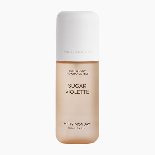 A bottle of Misty Monday Sugar Violette hair and body fragrance mist, featuring a warm beige body and a white cap, centered on a light gray background.