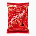 A red bag of Lindt Lindor milk chocolate christmas tree ornaments with gold and white decorative graphics, photographed on a plain light gray background.