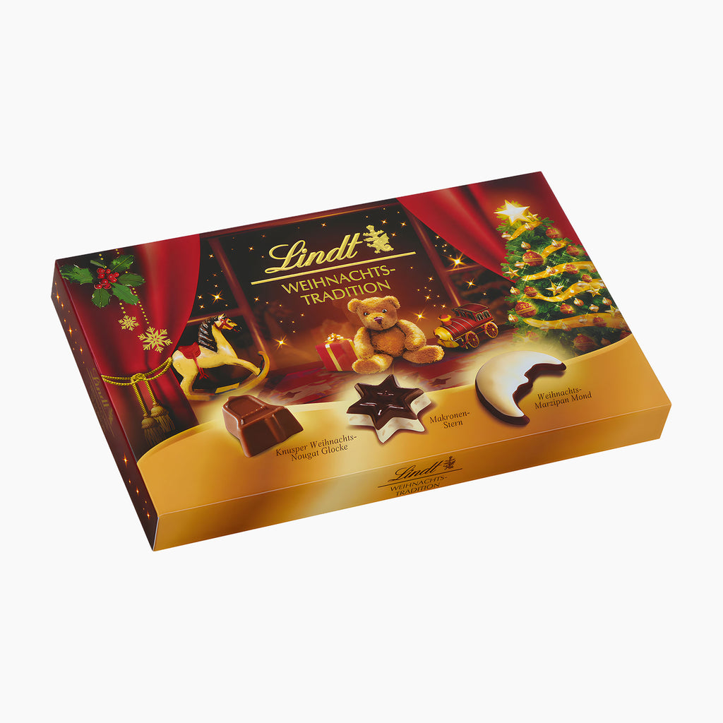 A box of Lindt Christmas Traditions chocolate pralines shown at an angle on a clean white background. The packaging features festive illustrations including a teddy bear, a rocking horse, a Christmas tree, and a golden gradient base, with the Lindt brand name clearly visible.