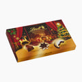 A box of Lindt Christmas Traditions chocolate pralines shown at an angle on a clean white background. The packaging features festive illustrations including a teddy bear, a rocking horse, a Christmas tree, and a golden gradient base, with the Lindt brand name clearly visible.