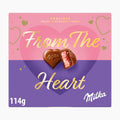 A square box of Milka Pralines Velvet Strawberry Creme, featuring a pink and purple heart design with gold lettering that reads 'From The Heart' and two heart-shaped pralines on the front.