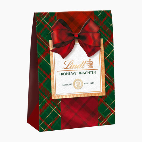 Lindt Karo Royal chocolate pralines bag with a red and green tartan pattern, a large red bow, and a central white label with gold text on a light gray background.