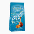 A 100g bag of Lindt Lindor Caramel & Salt milk chocolate pralines on a light gray background.