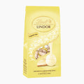 A 100g bag of Lindt Lindor Cheesecake white chocolate pralines in a pale yellow bag with white floral details and a photo of the filled chocolate pieces.