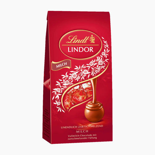 A 100g package of Lindt Lindor Milk Chocolate pralines with a rich red background, featuring the Lindt logo, white floral illustrations, and a golden swirl leading to a milk chocolate piece.