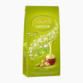 A 100g pack of Lindt Lindor Pistachio chocolate pralines, featuring a bright green bag with illustrations of pistachio nuts, white flowers, and a golden drizzle of chocolate.