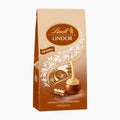 A 100g pack of Lindt Lindor Tiramisu chocolate pralines, featuring a beige and brown stand-up bag with white floral graphics, a gold-dripping motif, and an illustration of a chocolate piece with a slice of a tiramisu.