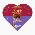 A heart-shaped Milka chocolate pralines box with a red top half and purple bottom half, decorated with gold heart outlines and the words 'Love You' in gold script. Two Milka milk chocolate pralines are shown in the center, with '8 Milka' printed near the bottom.