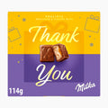 A square chocolate box design for Pralines Milk Crème & Caramel Bliss, with a yellow upper half reading 'Thank' and a purple lower half reading 'You', plus the Milka brand name and 114g text. Two chocolate pralines are shown in the center.