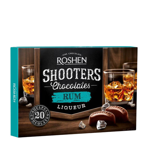 Roshen Shooters Chocolates Rum Liqueur packaging with glasses of rum and chocolates on a wooden surface.