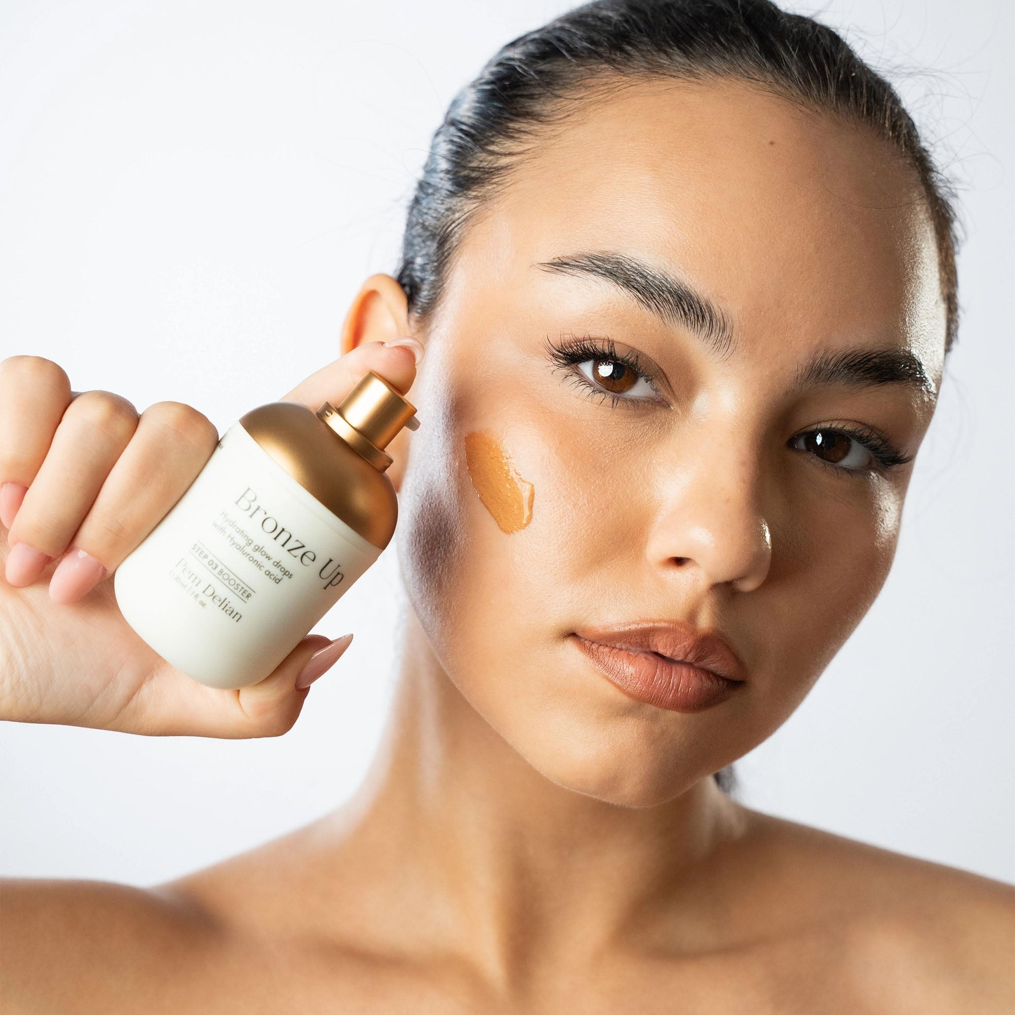Woman applying a cosmetic product to her face with a bottle labeled 'Bronze Up'.