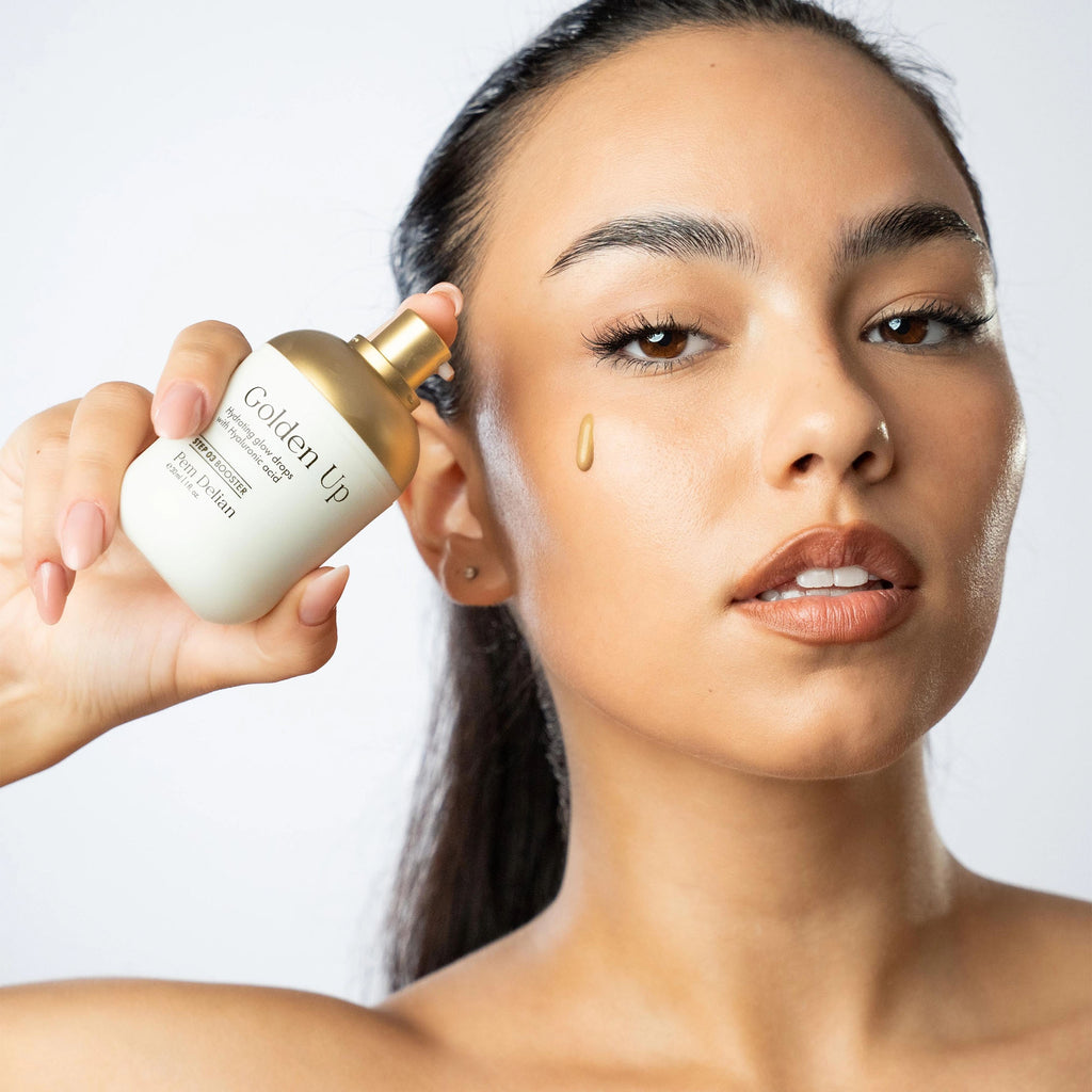 Woman applying Golden Up skincare product to her face with a droplet on her cheek.