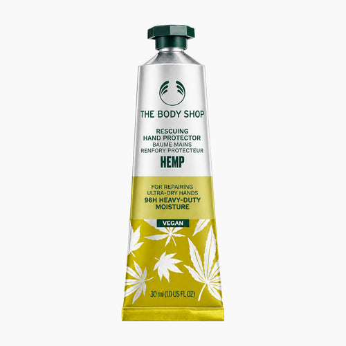 A squeeze tube of The Body Shop Hemp Rescuing Hand Protector hand balm, featuring a silver upper section, a yellow lower section with white hemp leaf illustrations, and a dark green cap, set against a plain white background.
