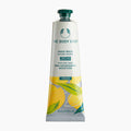 A squeeze tube of The Body Shop Mango Hand Balm, featuring a white tube with green and yellow mango illustrations, a dark green cap, and teal text on a light gray background.