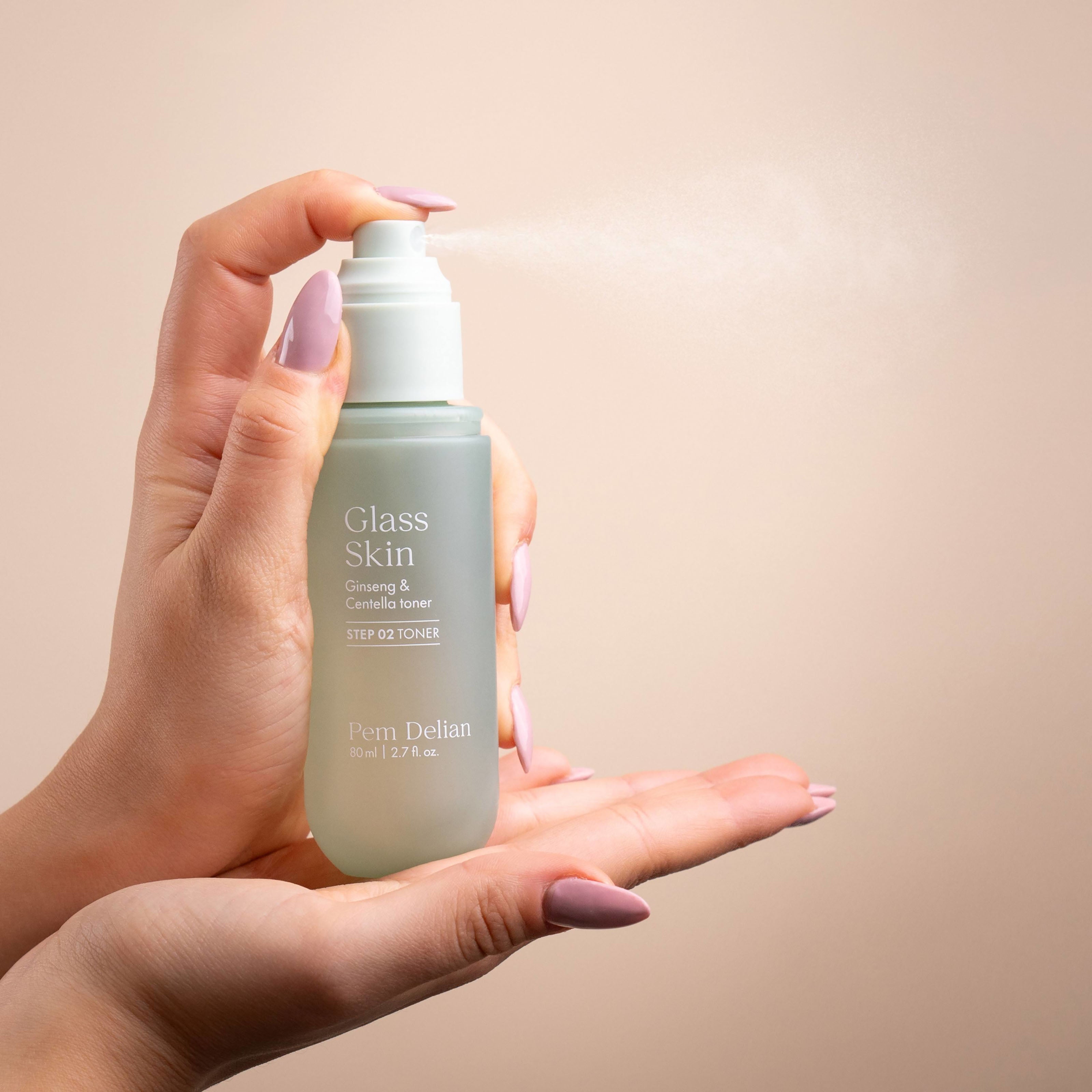 Hand holding a toner bottle labeled 'Glass Skin' against a beige background