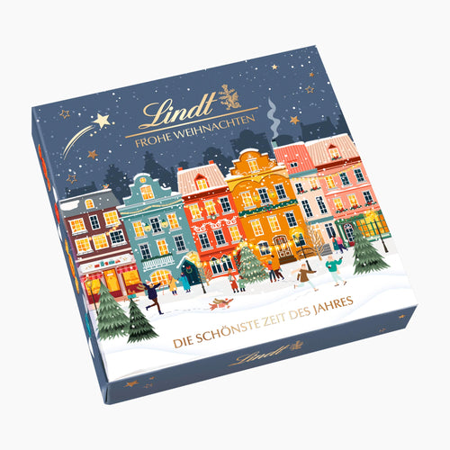 Lindt Winter Houses chocolate pralines gift box featuring a colorful winter town illustration on a dark blue background, photographed on a light gray studio background.